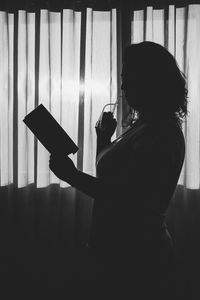 Side view of silhouette woman holing book standing at home