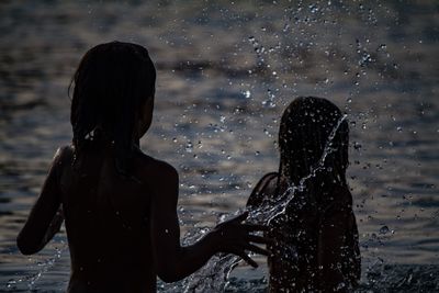 Silhouette sisters splashing water in sea