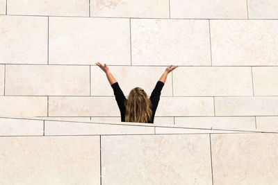 Rear view of woman with arms raised standing amidst wall
