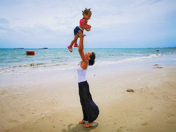 Mother throws her child into the air with joy on a beautiful beach