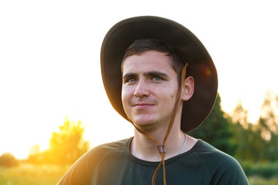 Young man smiling farmer in cowboy hat at agricultural field on sunset with sun flare. closeup 