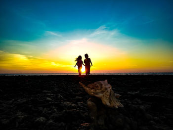 Silhouette people on beach against sky during sunset