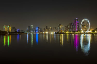 Illuminated buildings by river against sky at night