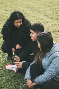 Happy family in the park sitting, watching and sharing smartphones