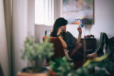 Young woman talking on phone while sitting on sofa at home