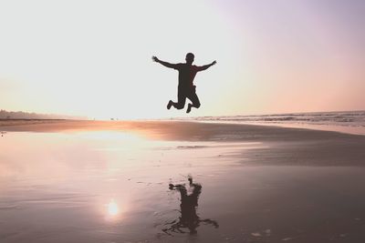 Man jumping at beach against sky during sunset