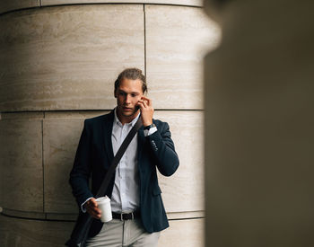 Businessman taking on phone while standing against wall