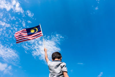 Low angle view of boy holding flag against blue sky