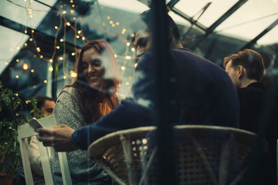 Low angle view of man showing smart phone to female friend while sitting in conservatory during dinner party