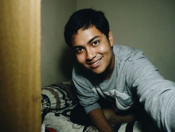 Portrait of smiling young man sitting on bed at home