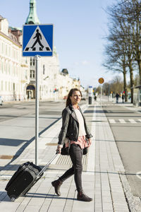 Businesswoman pulling luggage while crossing road in city