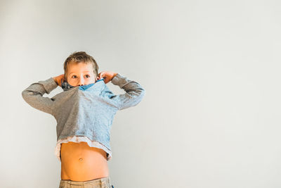 Boy removing t-shirt while standing against white background