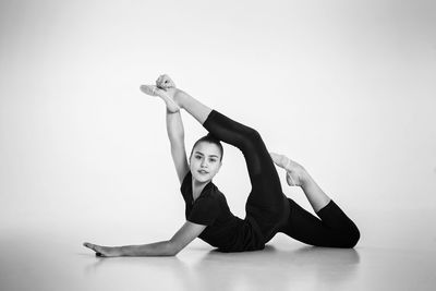 A girl from rhythmic gymnastics in a bodysuit shows stretching lying on the floor