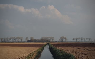 Empty road amidst field against sky