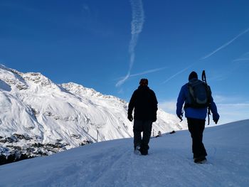 Rear view of man walking on snowcapped mountain against clear blue sky