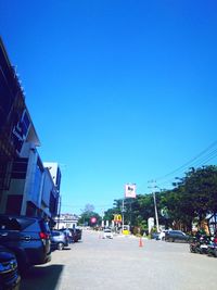 Cars on road by buildings against clear blue sky