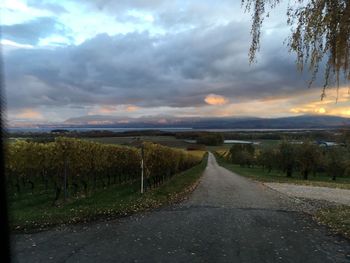 Road passing through landscape against storm clouds