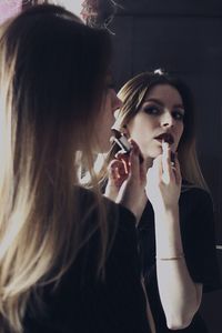 Woman applying lipstick while looking in mirror