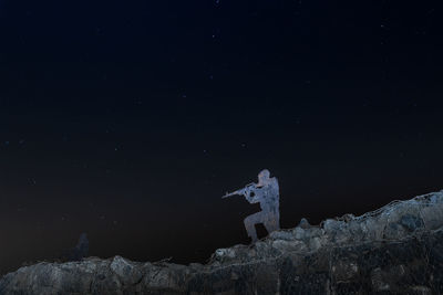 Low angle view of man standing on rock against sky at night