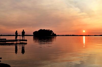 Silhouette people standing by lake against sky during sunset