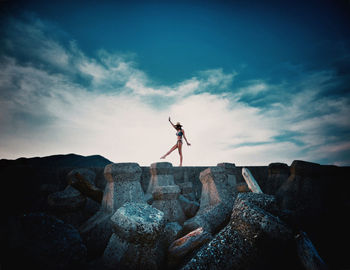 Woman wearing bikini walking on rocks at beach against sky