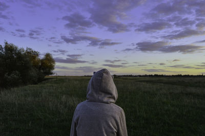 Rear view of man standing on field against sky during sunset