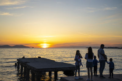 People standing on beach against sky during sunset