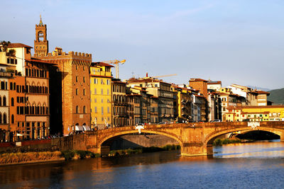 Arch bridges over arno river by buildings against sky