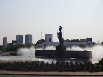 Statue by fountain against buildings in city against clear sky
