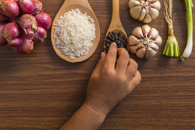 Cropped hand of child holding black peppercorns by ingredients on table