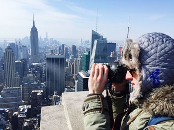 Photographer photographing by cityscape against sky