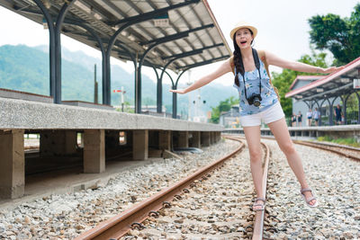 Young woman with arms outstretched walking on railroad tracks