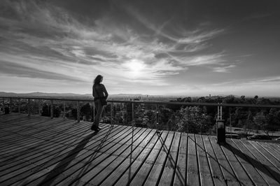 Rear view of man on wooden pier over river against sky