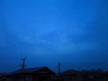 Low angle view of silhouette electricity pylon against blue sky