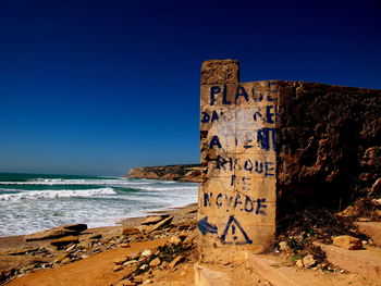 Information sign on beach against clear blue sky