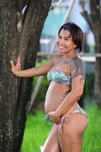 Portrait of pregnant woman standing by tree trunk