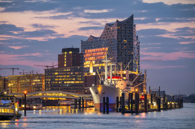 Illuminated buildings at waterfront during sunset