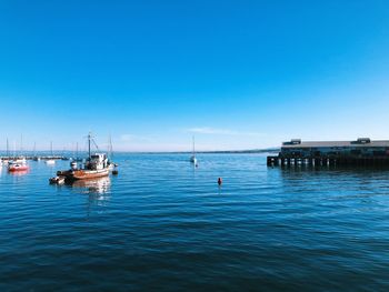 Boats sailing in sea against clear blue sky