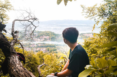 Young man looking at tree against sky