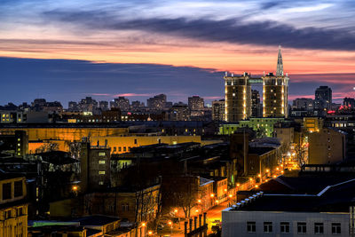 Illuminated buildings in city against sky at sunset