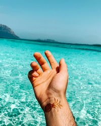 Close-up of hand against sea against sky