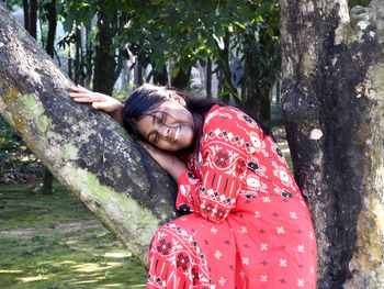 Portrait of young woman sitting on tree trunk