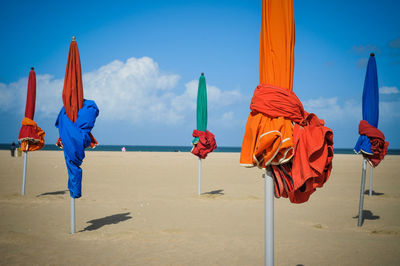 Colorful closed parasols against sky at sandy beach on sunny day