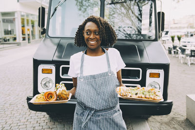 Smiling female owner holding indian food plate while looking away in city