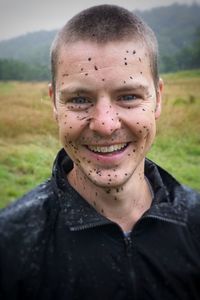 Close-up portrait of cheerful young man with dirty face standing on field