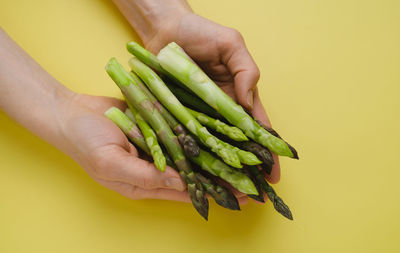 Cropped hand of person holding carrots on yellow background