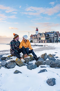 Rocks sitting on snow covered shore against sky