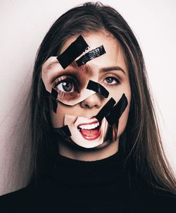 Close-up portrait of sad young woman with adhesive tape and photographs against wall