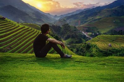 Man sitting on field against mountains