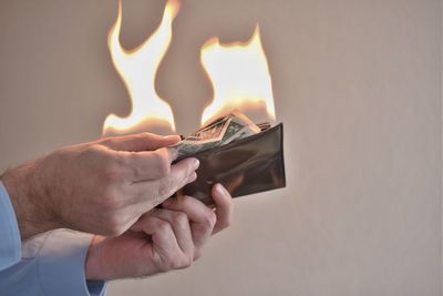 Cropped hands of man removing burning paper currencies from wallet